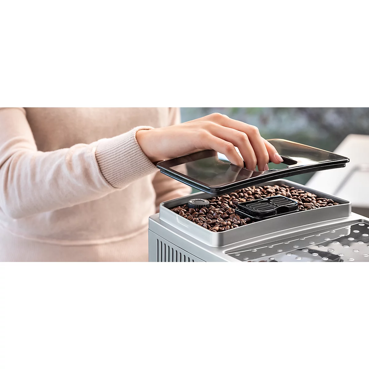 Une personne ouvre le couvercle du bac à grains d'une machine à café pour y verser des grains de café.