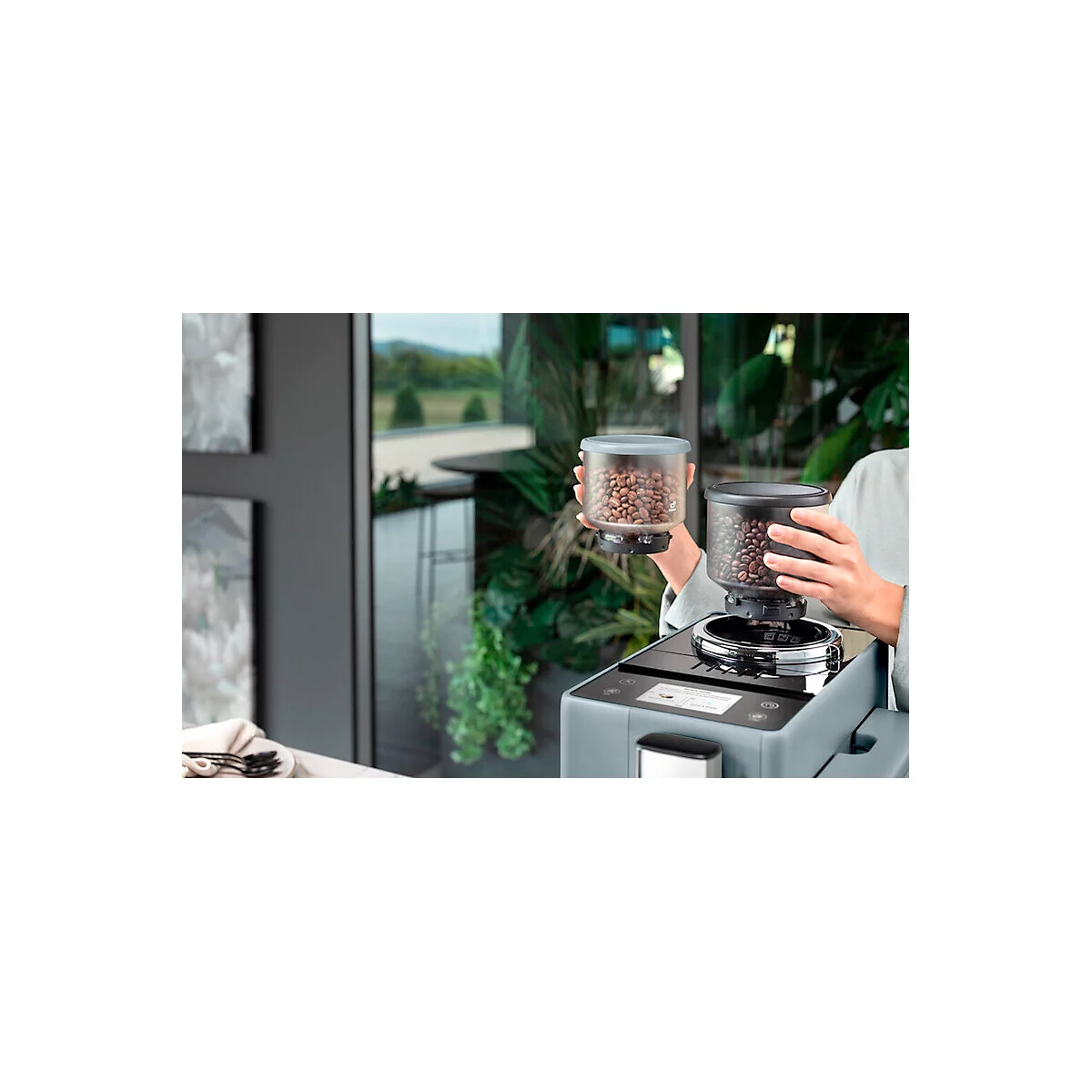 Une personne tient un récipient à grains de café. Un deuxième récipient est placé sur une machine à café.