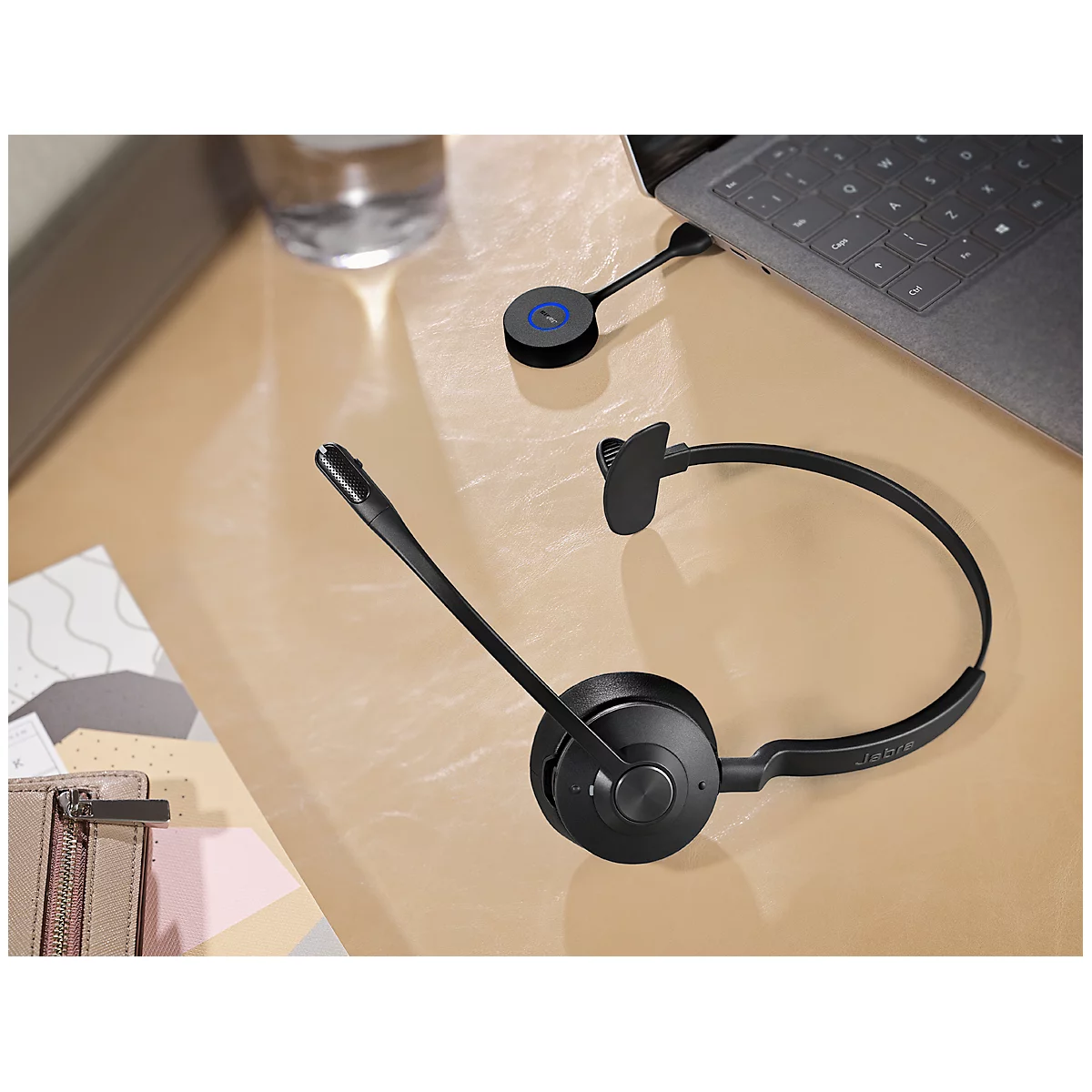Black headset and accessories on a table. Laptop in the background.