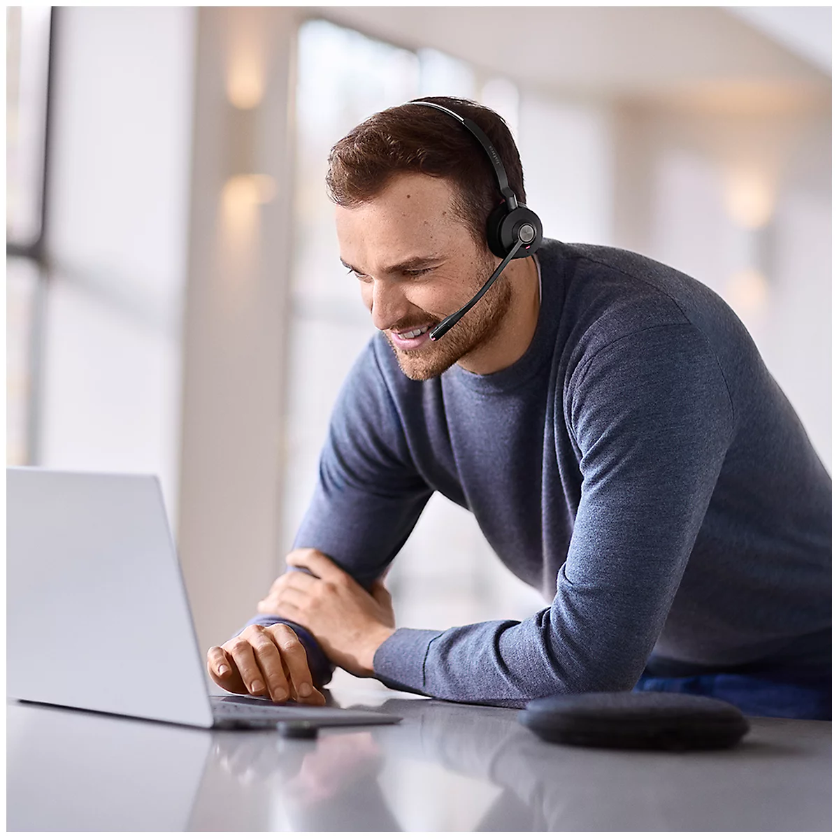 A man wearing a headset, smiling and looking at a laptop.