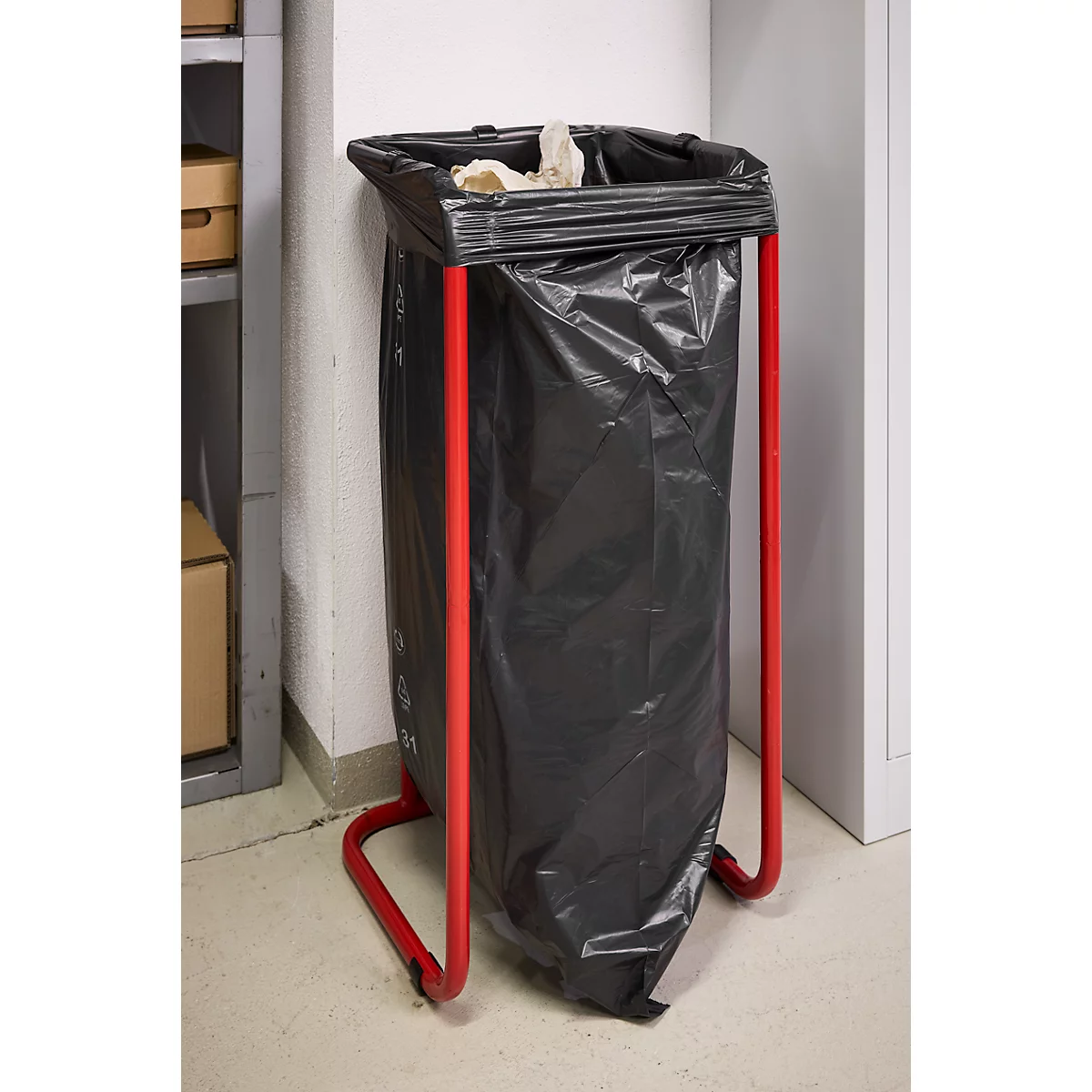 Schwarzer Müllsack in einem roten Gestell, gefüllt mit Papier. Der Hintergrund ist weiß.