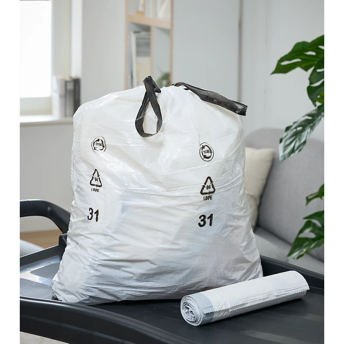 Witte vuilniszak met handvat, gevuld. Gemarkeerd met 31 en een recyclingsymbool. Daarnaast een rol nieuwe vuilniszakken.