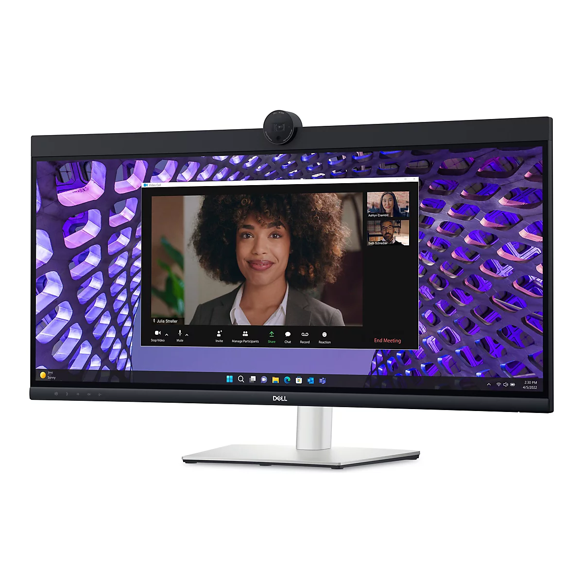 Un moniteur Dell avec une webcam intégrée affiche un appel vidéo. Une femme aux cheveux bouclés parle, avec deux autres participants visibles dans la fenêtre. L'arrière-plan de l'écran est un motif abstrait.