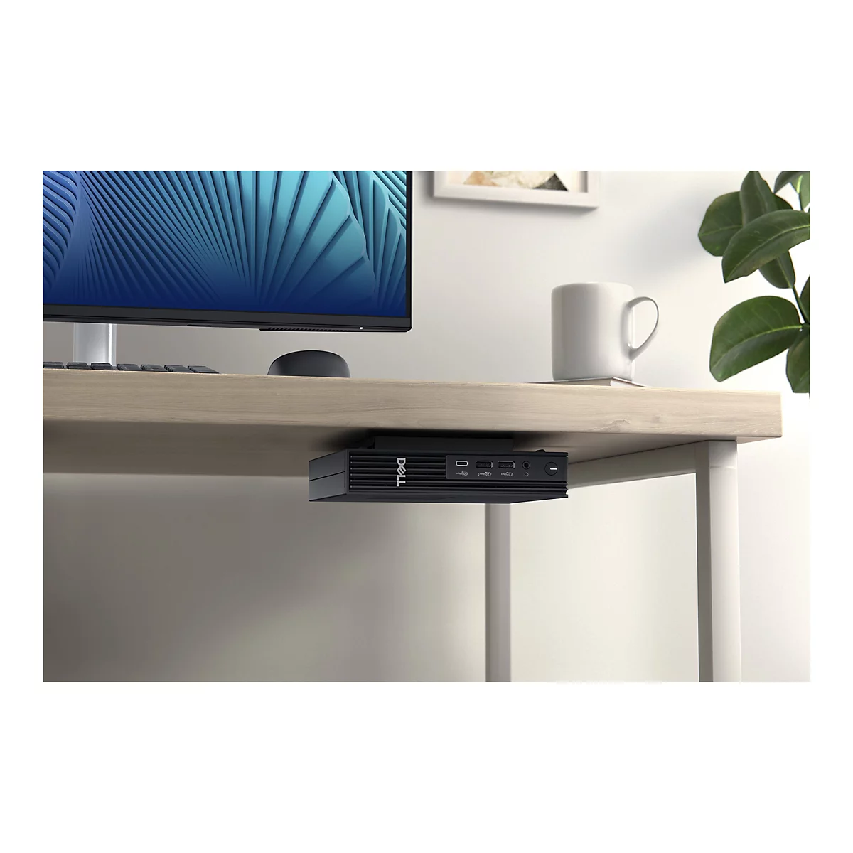 Ein schwarzer Dell-Mini-PC ist unter einem Holzschreibtisch montiert. Auf dem Schreibtisch befinden sich ein Monitor mit blauem Muster, eine Maus, eine Kaffeetasse und Grünpflanzen.