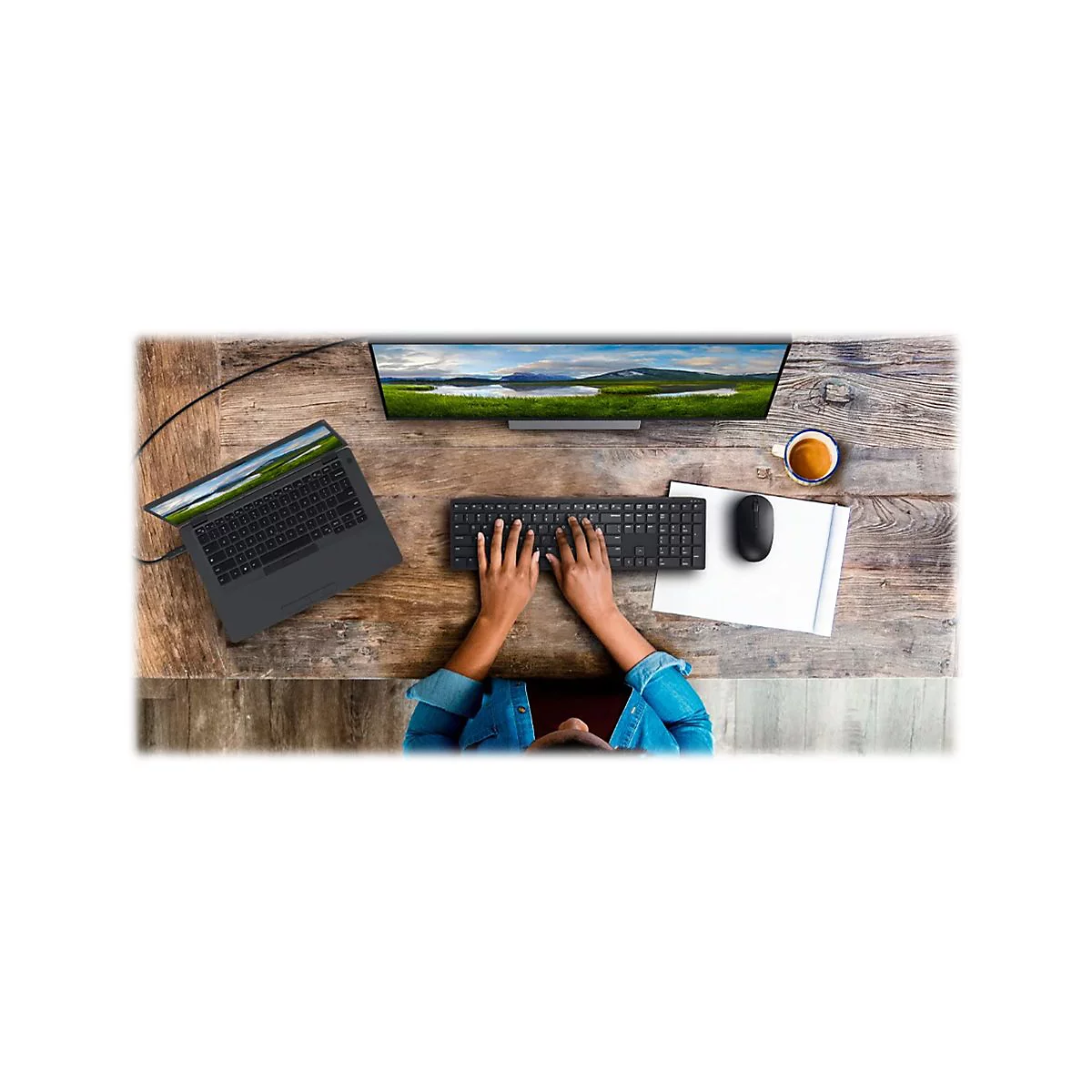Draufsicht auf einen Schreibtisch mit Laptop, Tastatur, Maus, Monitor und einer Person, die die Tastatur benutzt.