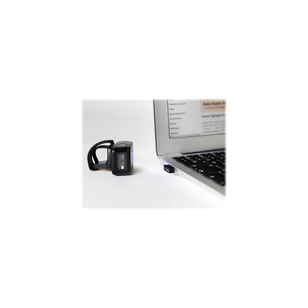 Ein schwarzer Barcode-Scanner mit Armband neben einem Laptop mit eingestecktem Bluetooth-Adapter.