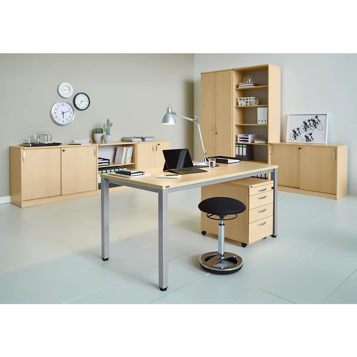 Office with desk, laptop, chair, and cabinets. On the wall: clocks, picture and a small plant.