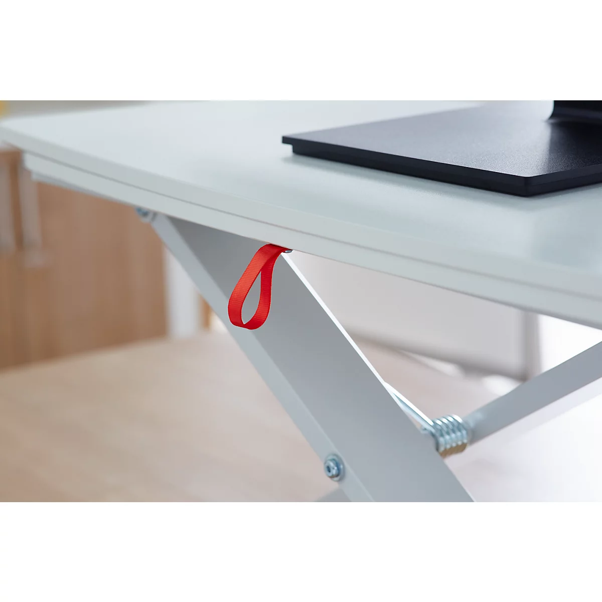 Close-up of a white desk with a red loop. The desk has a black rectangle on its surface and a silver metal construction.