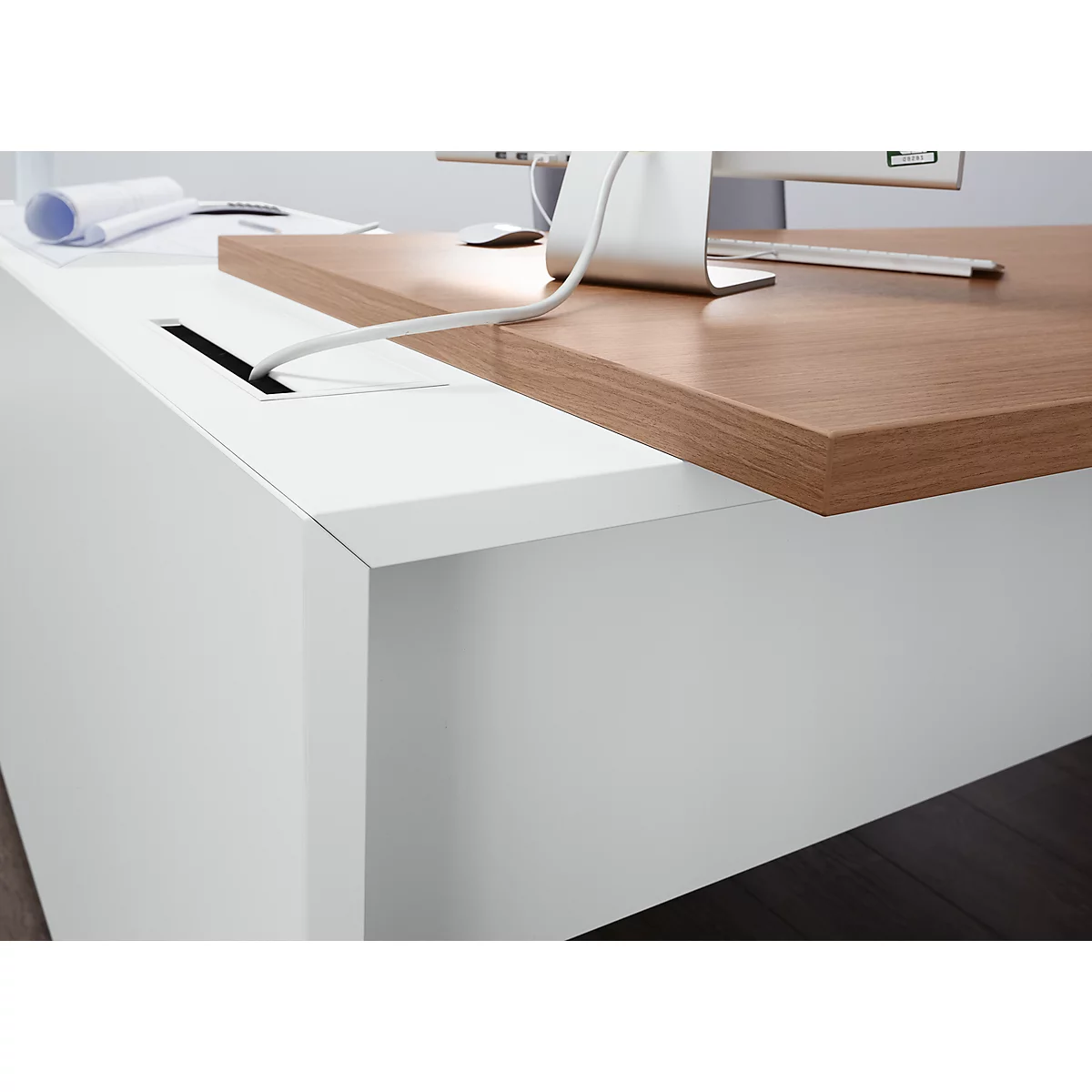 Close-up of a white desk with a brown wooden top. A cable is being fed into an opening.