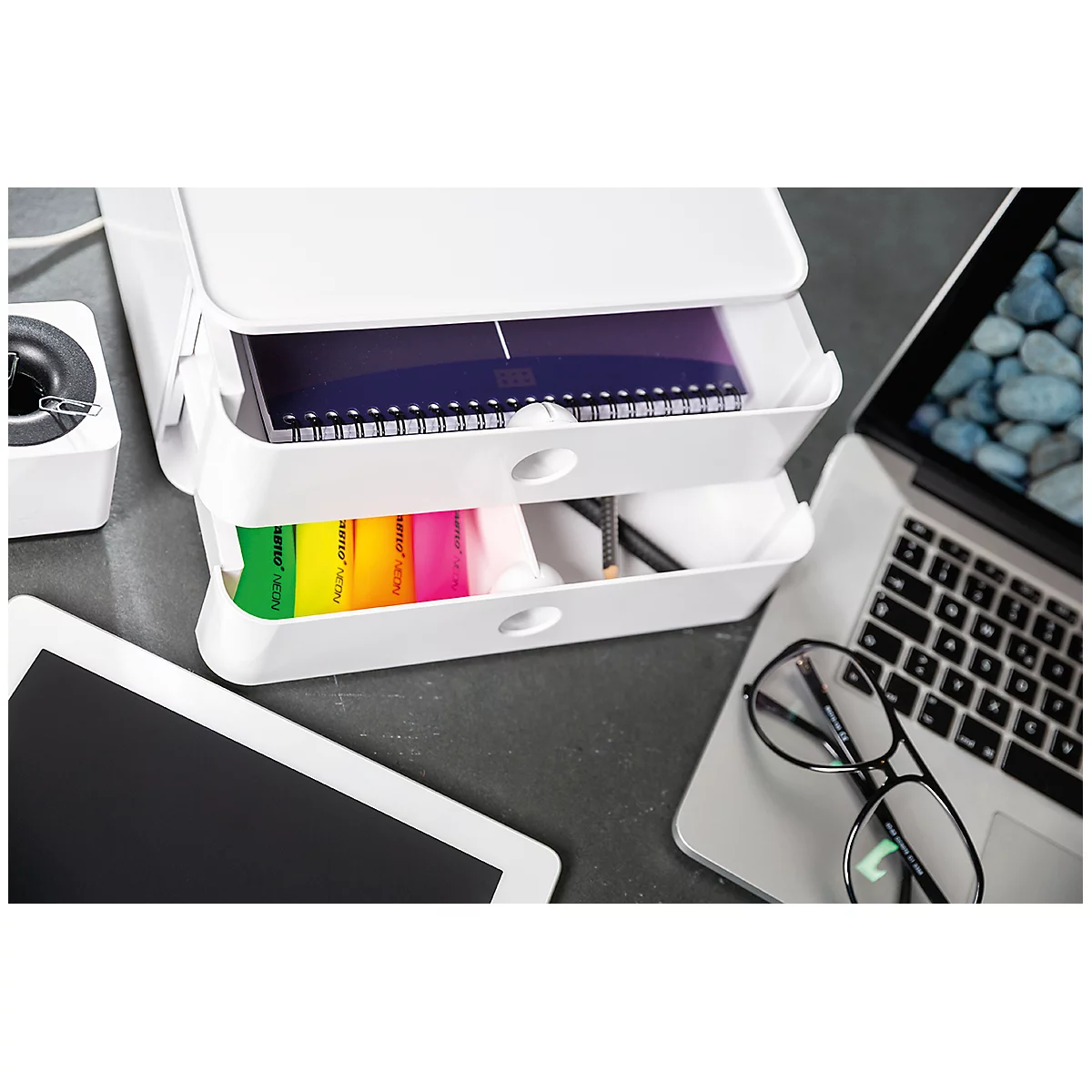 White desk organizer with open drawers. Inside: notebook, pens, highlighters. Next to it: laptop, tablet, glasses.