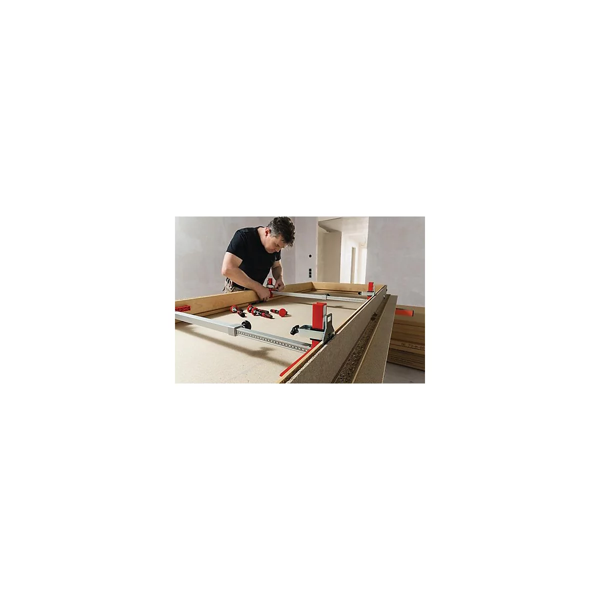Een man bouwt een houten frame met gereedschap. Rode en zilveren klemmen en gereedschap liggen op het oppervlak.