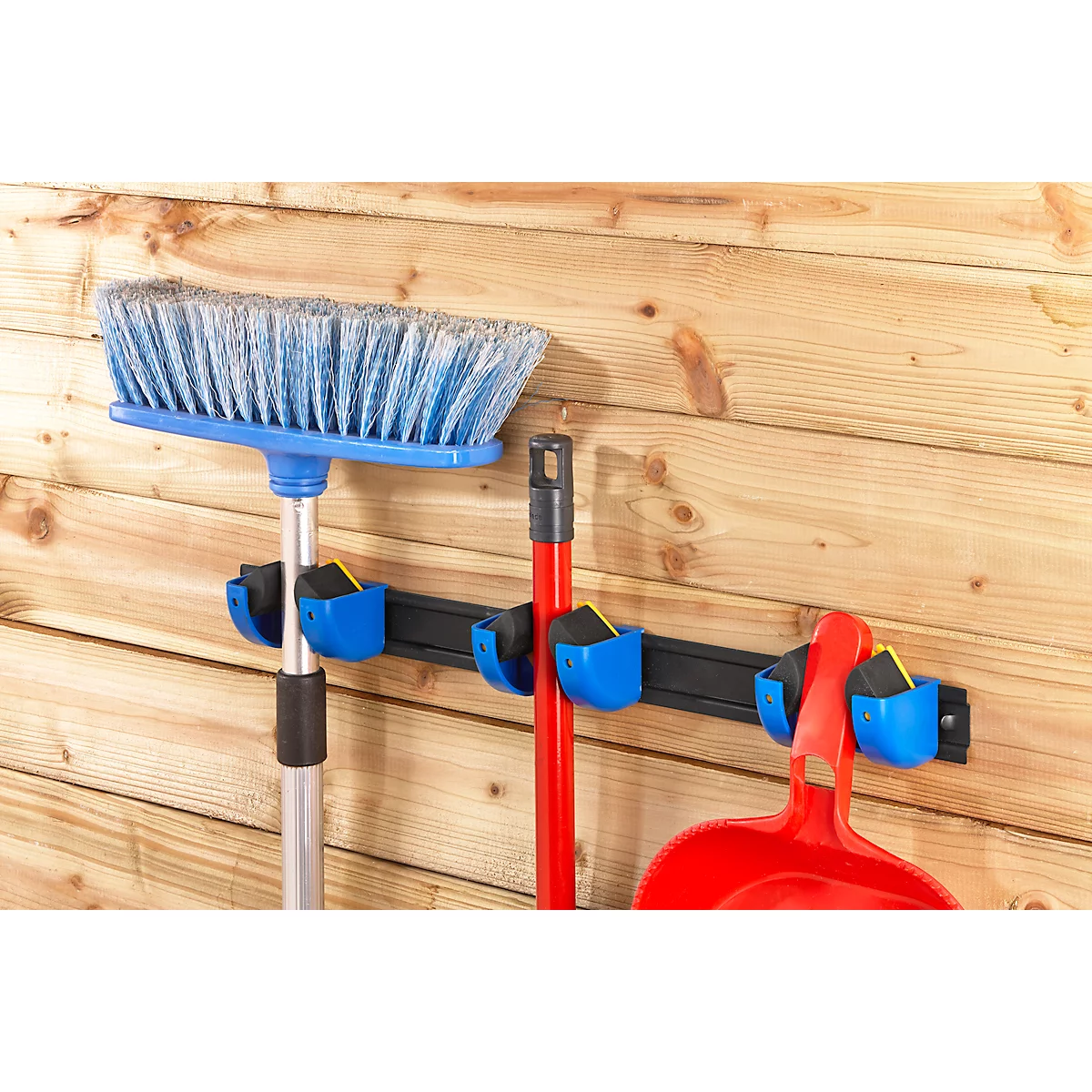 Broom, shovel and dustpan set in blue holders on a wooden plank wall.