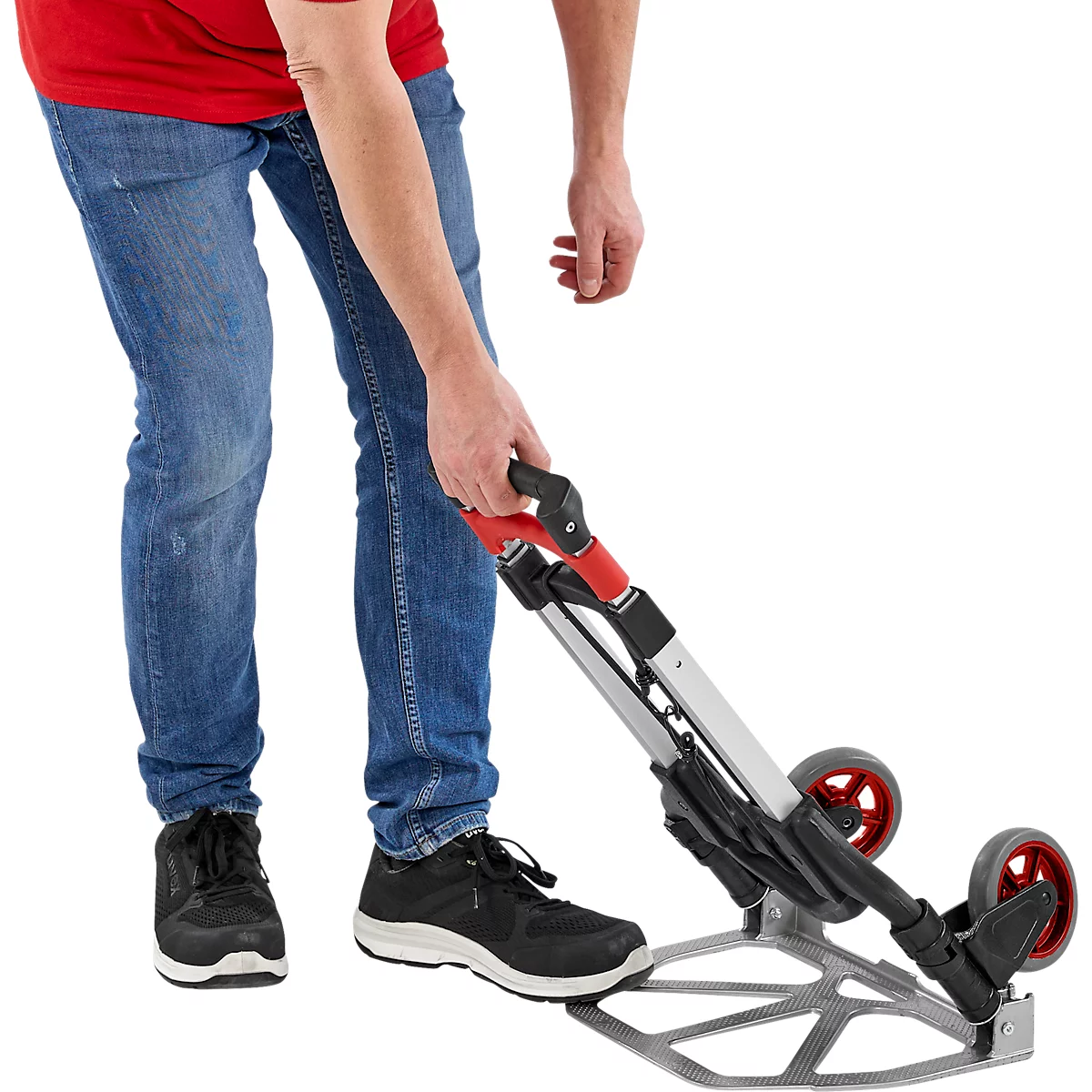 Un homme en jean et chemise rouge utilise un chariot de transport pliable.