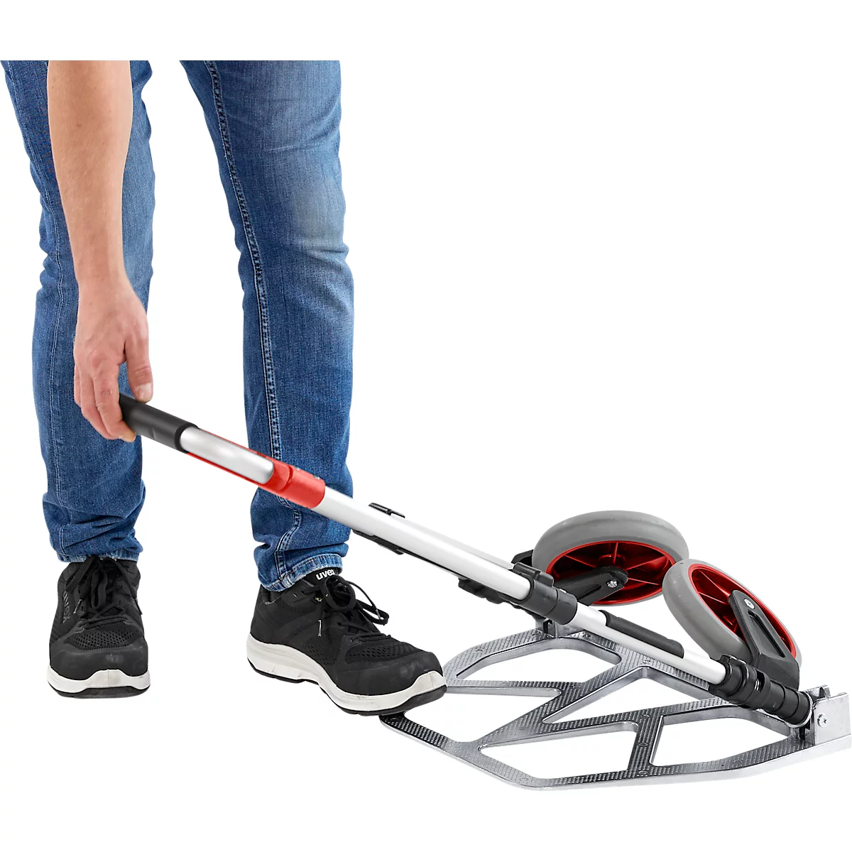 Personne en jean et chaussures noires utilisant un chariot argenté avec des roues grises et rouges.