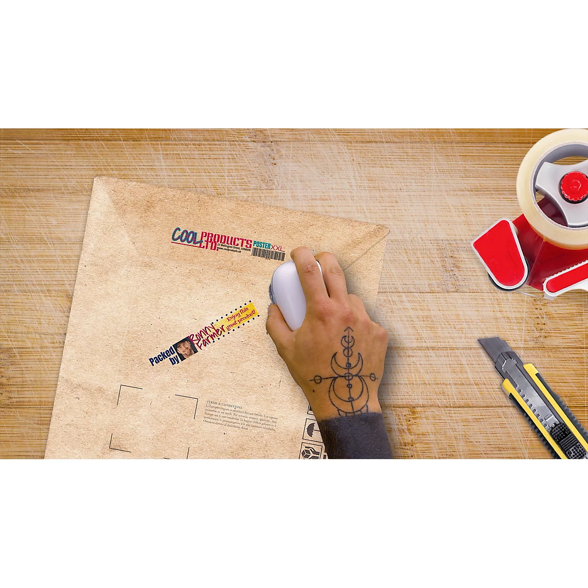 Hand with tattoo holding a mouse over a shipping envelope. Adhesive labels on the envelope, next to it tape and cutter knife.