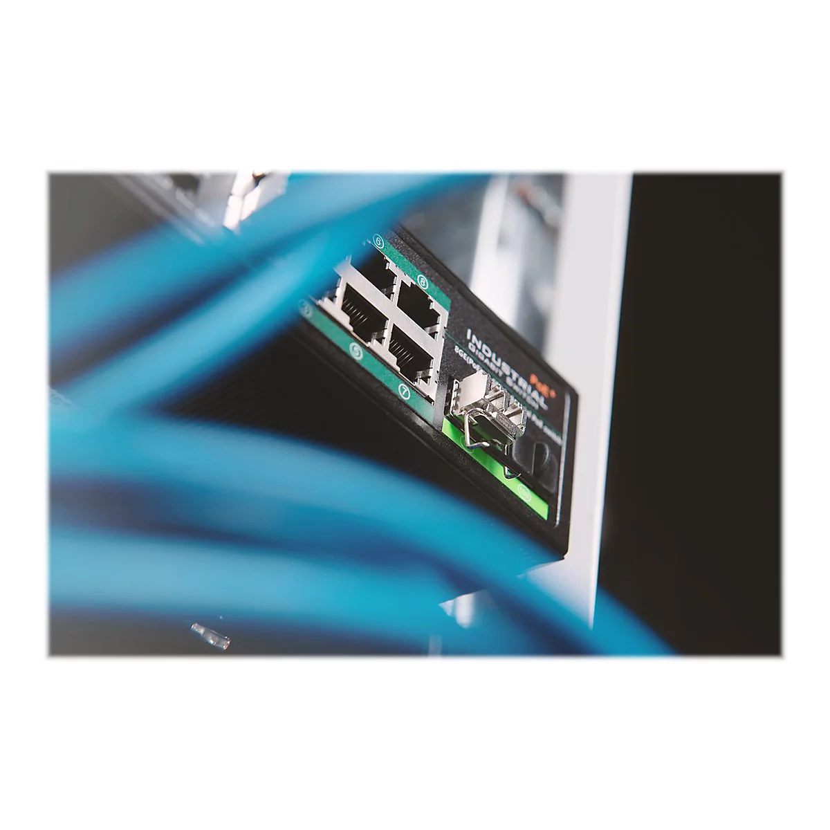 Ein schwarzer Industrial Ethernet Switch mit AnschlÃ¼ssen, darÃ¼ber blaue Kabel. Die Szene ist leicht unscharf.