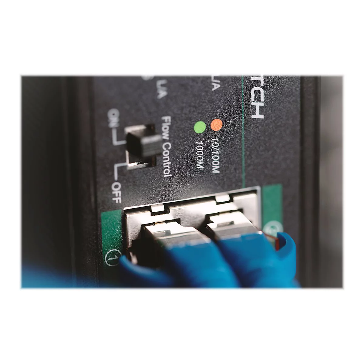 Nahaufnahme eines schwarzen Netzwerk Switches mit blauen Kabeln. Text: Flow Control, 10/100M, 1000M.