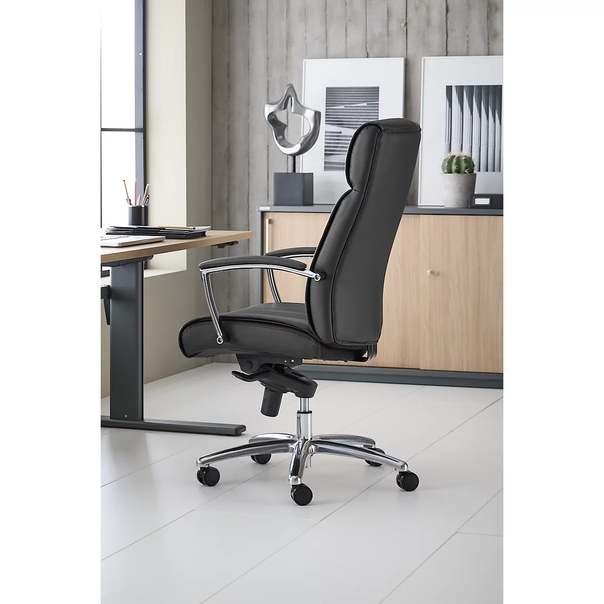 Zwarte bureaustoel met hoge rugleuning, zilveren frame, staat in een licht kantoor.