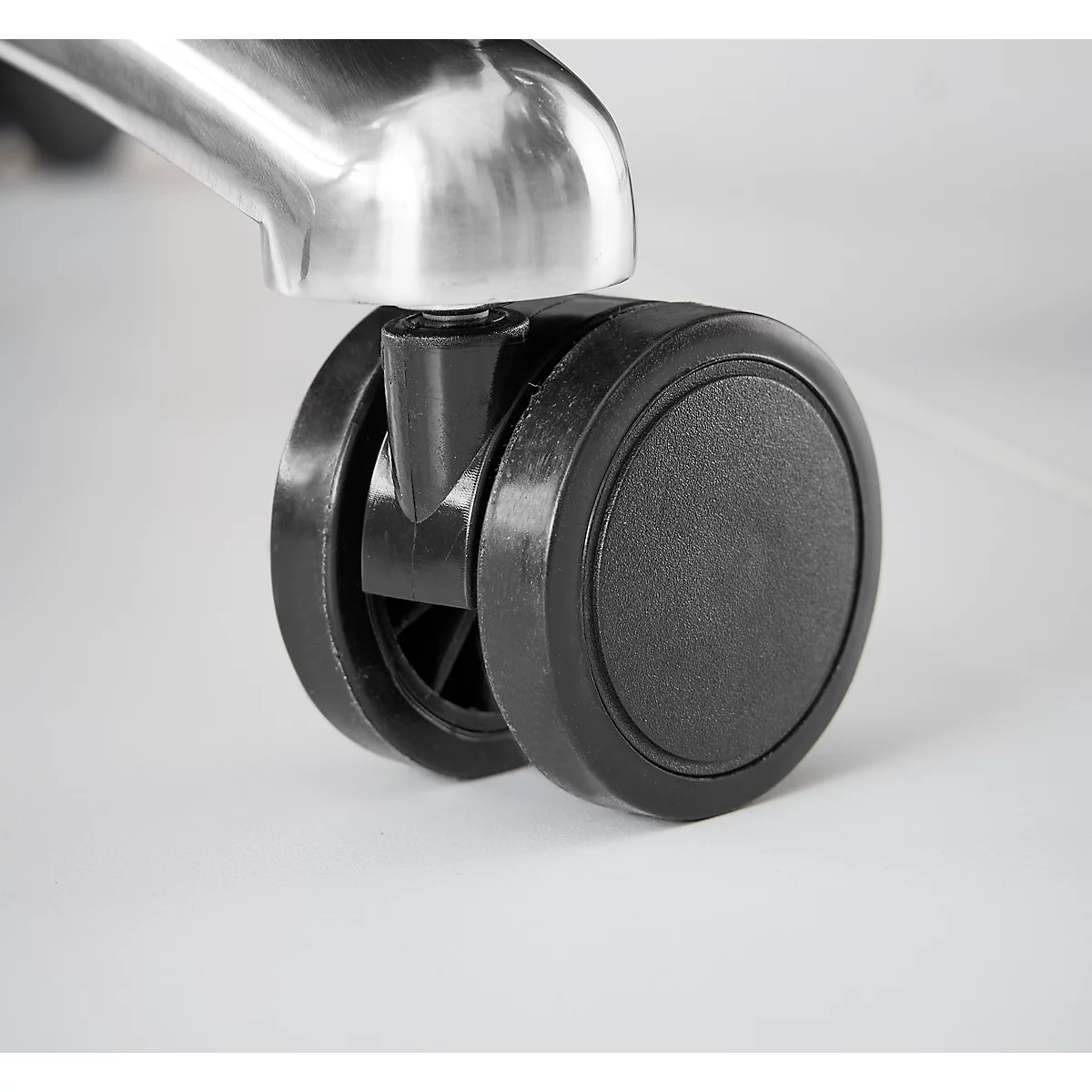 Close-up van een zwart stoelwiel onder een metalen stoelpoten.