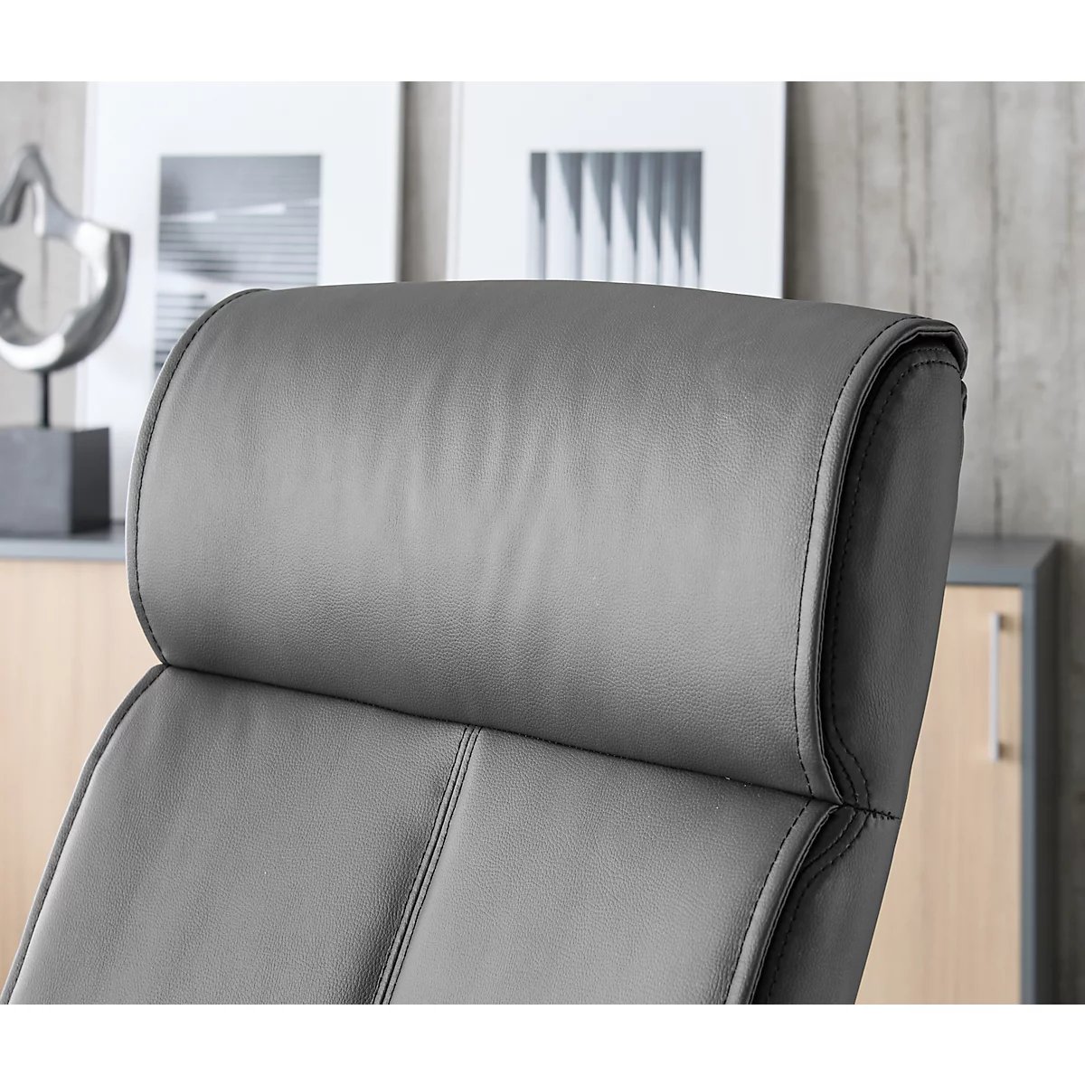 Close-up van een grijze bureaustoel bekleed met leer. De focus ligt op de hoofdsteun en de bovenrug, die een zachte, kussenvormige vorm hebben.