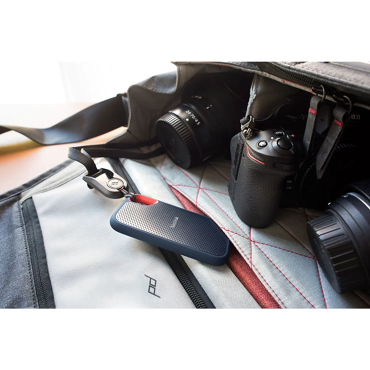 Disque dur bleu foncé avec un accent rouge sur un sac d'appareil photo. Plusieurs objectifs et un appareil photo en arrière-plan.