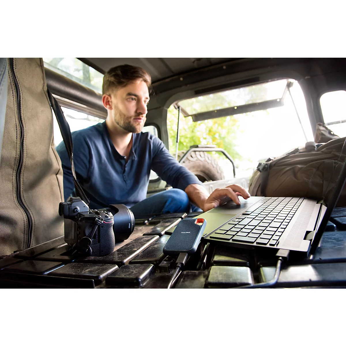 Homme avec ordinateur portable dans la voiture. Appareil photo, disque dur et sac à dos prêts. Travailler à l'extérieur.