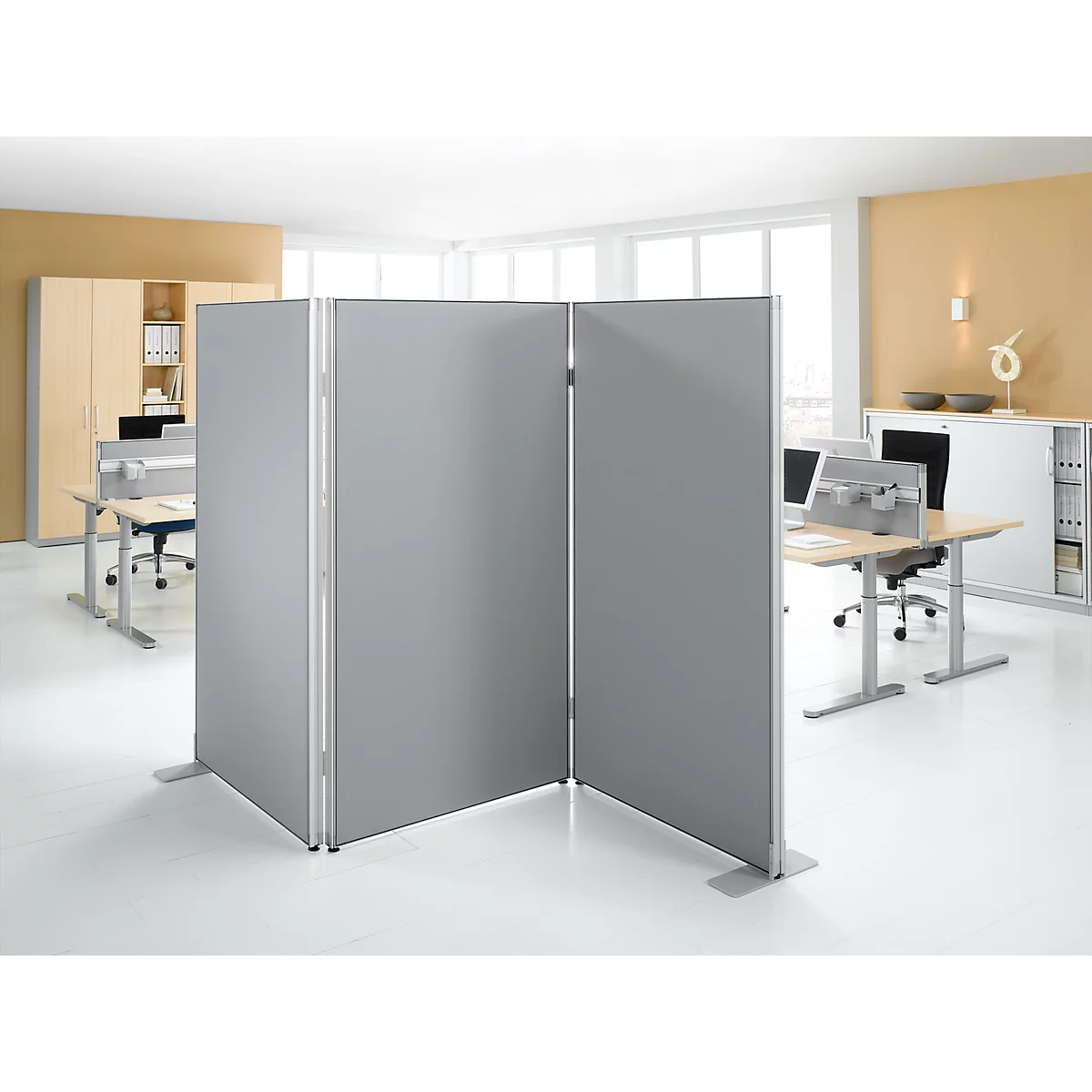 Gray room dividers in an office. Divided into three elements, with feet. Desks and windows in the background.