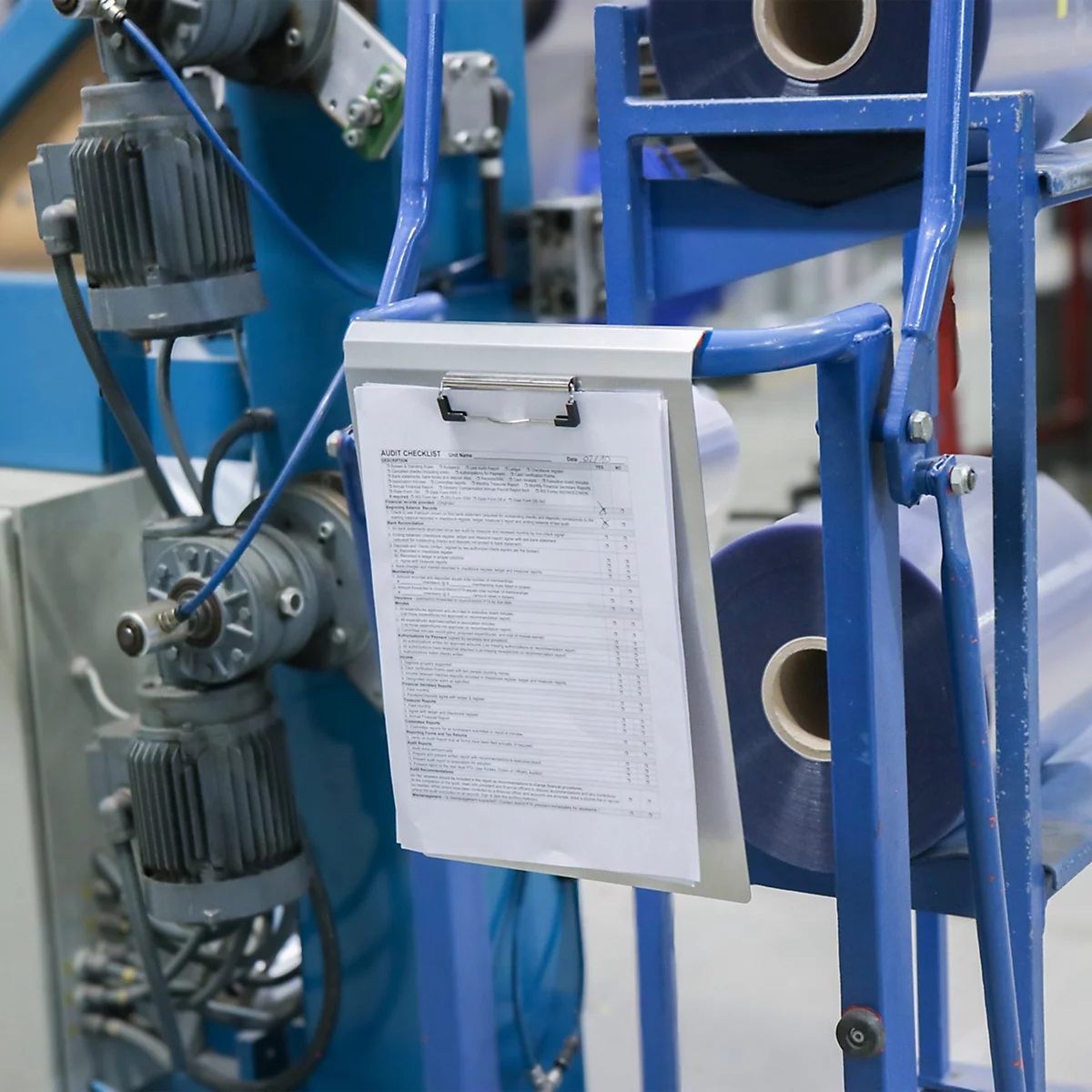 Klemmbrett mit Dokumenten hängt an einer industriellen blauen Produktionsmaschine.