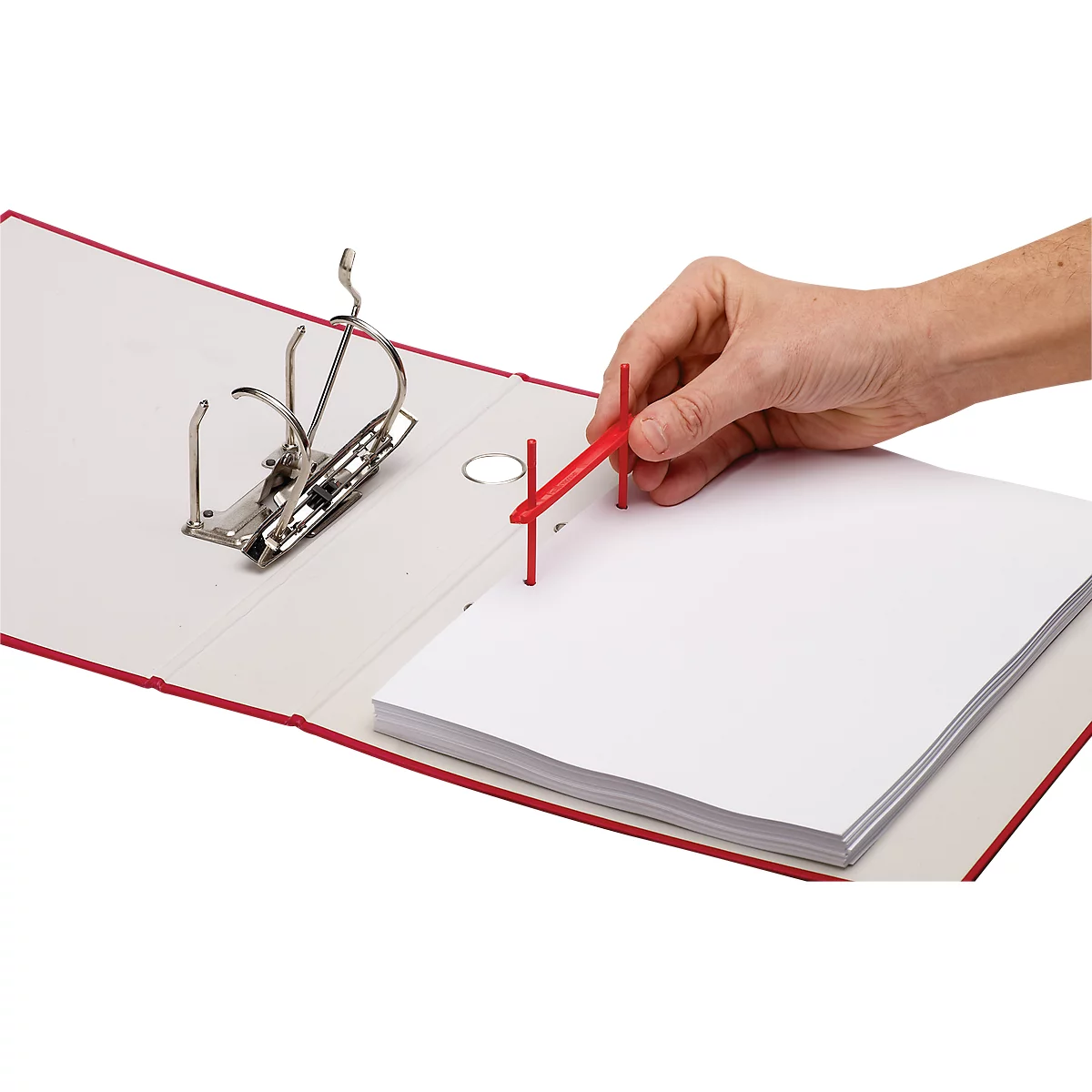 Red open binder with paper stack. Hand holding red tool for filing.