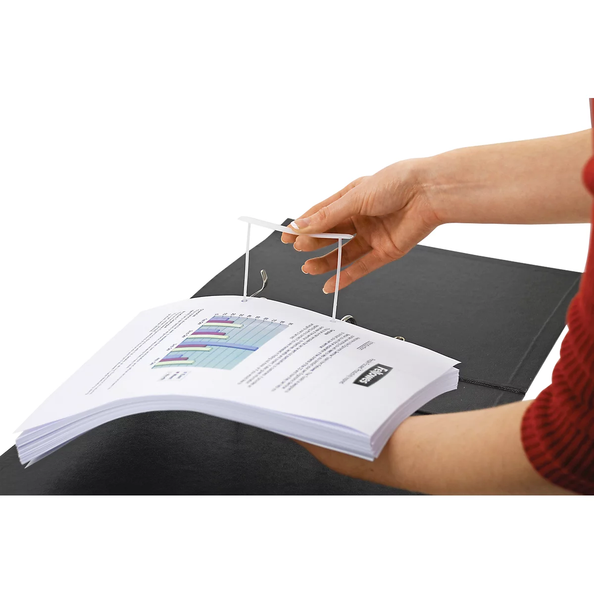 Person holding a binder with diagrams and a white holder. Red sleeve, black binder, white background.