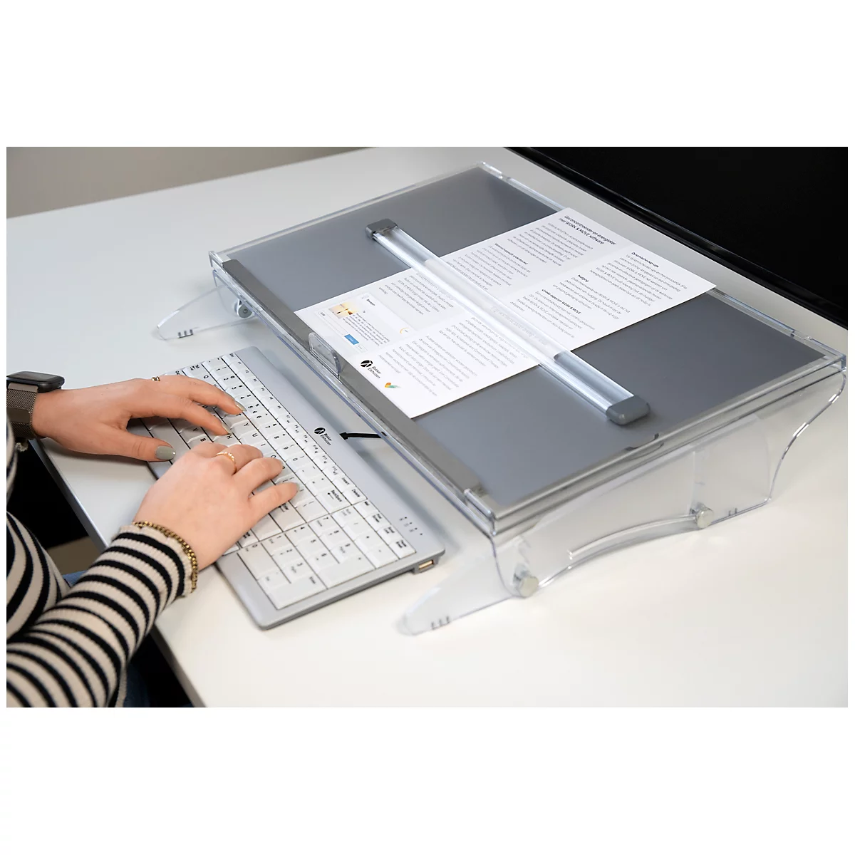 Person typing on a keyboard, with a document in a reading aid next to it.
