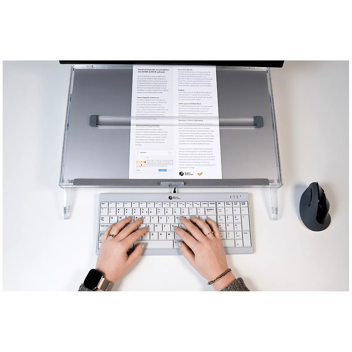 Person typing on a keyboard, in front of a document holder with text. A mouse is to the right.