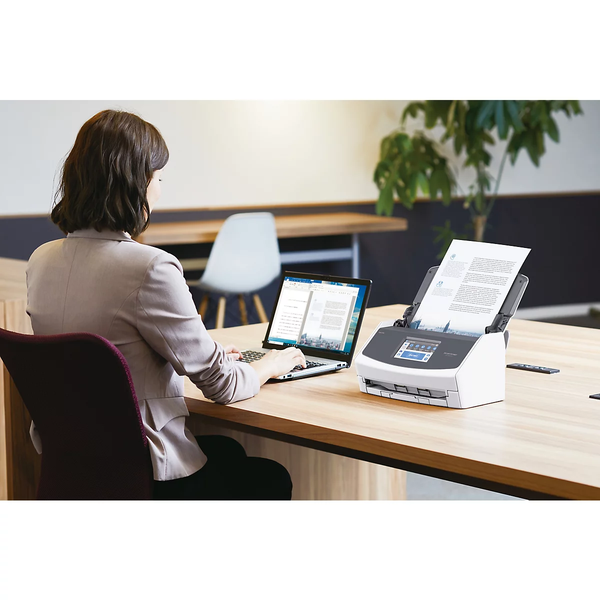 Een vrouw werkt aan een laptop en een scanner op een bureau. Een document wordt gescand.