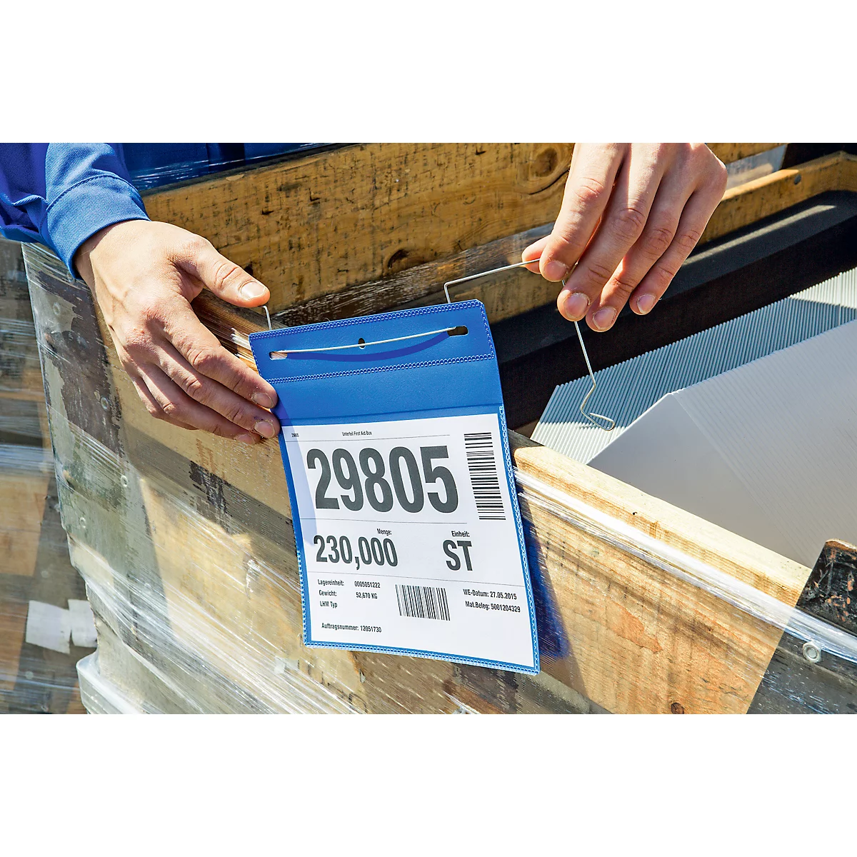 Eine Person hält ein blaues Etikett mit der Aufschrift "29805". Es ist an einem Holzgegenstand befestigt, im Hintergrund Holz und transparente Folie.
