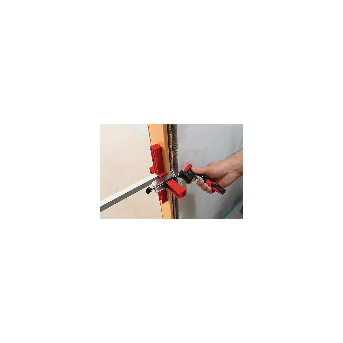 Hand holding tool to fix strips to wall and door frame. Red and black tool fixes silver strip.
