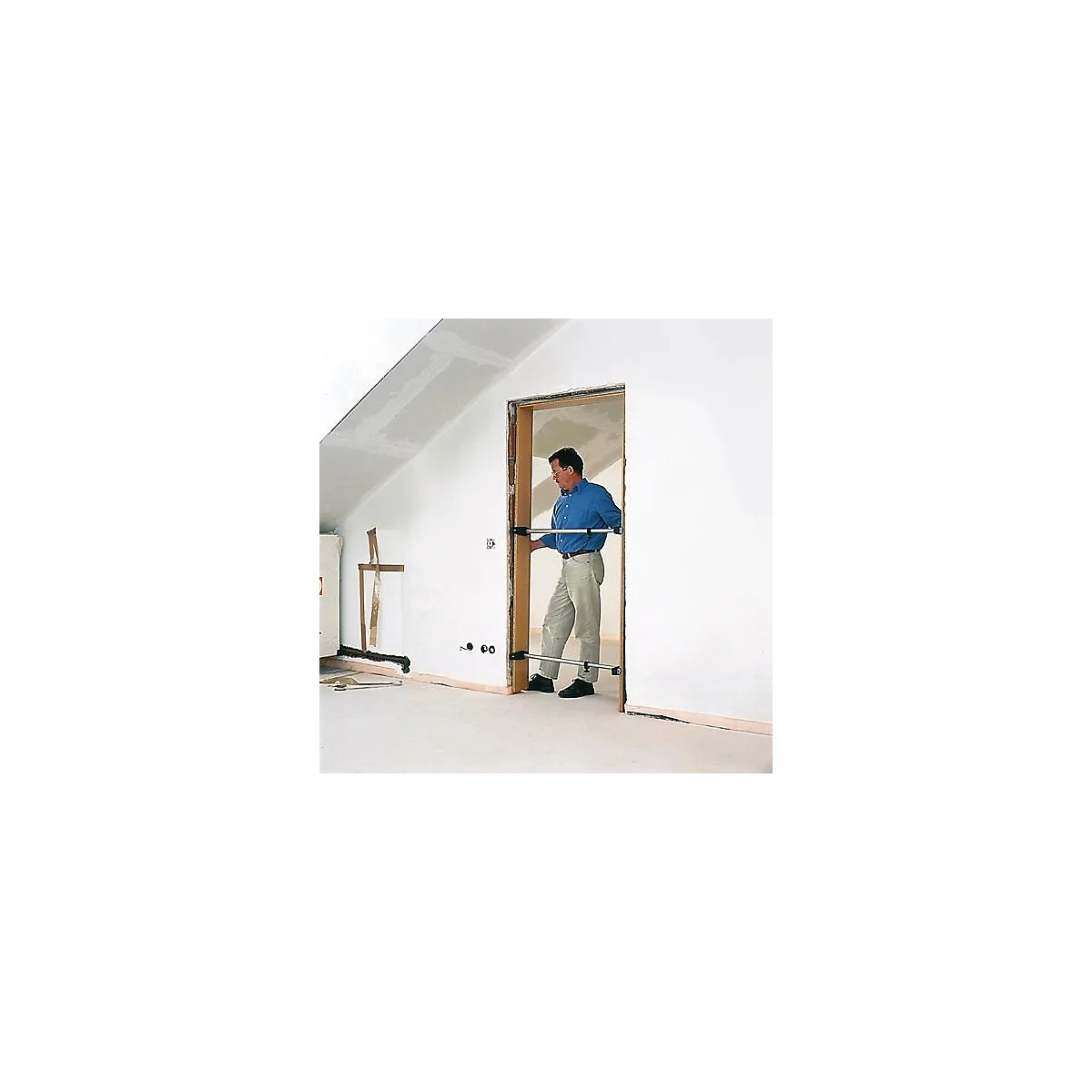 A man places a door frame with the help of two supports in an unfinished wall. Interior with sloping ceiling.