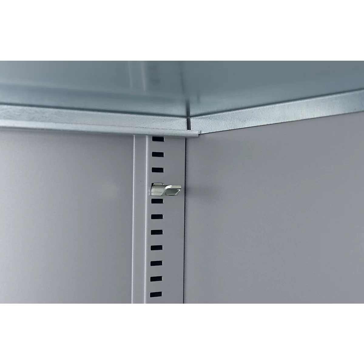 Detailweergave van een kastinterieur. Een zilveren kliksluiting op een grijze metalen wand, met een rij uitsparingen ernaast.