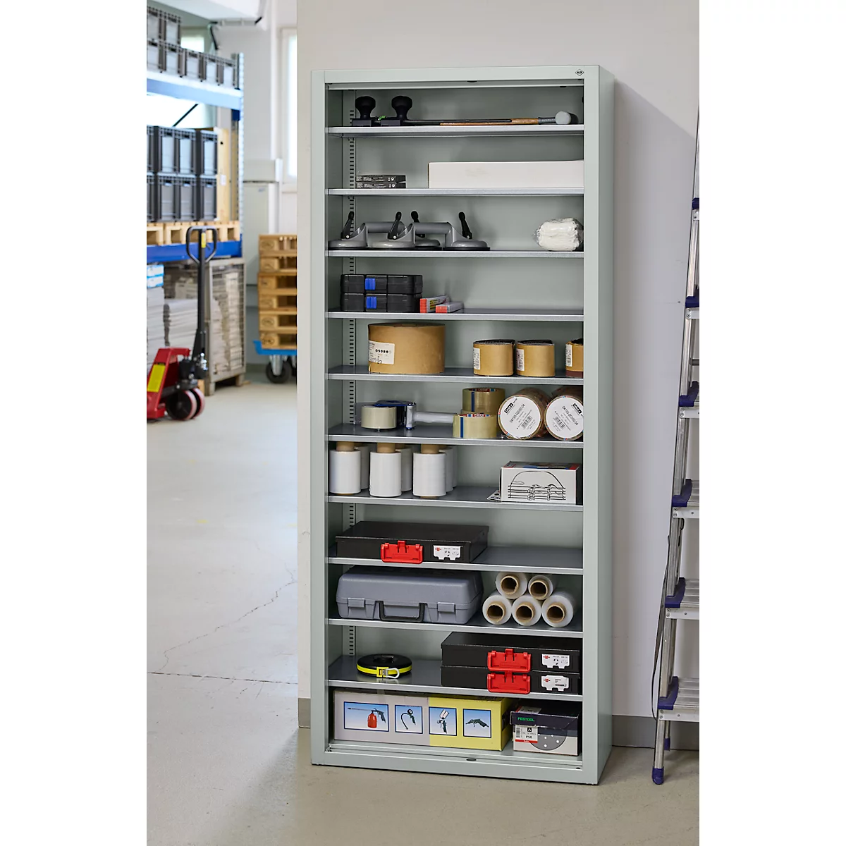 Grijs metalen kast met gereedschap, papierrollen, containers en dozen. In een werkomgeving.