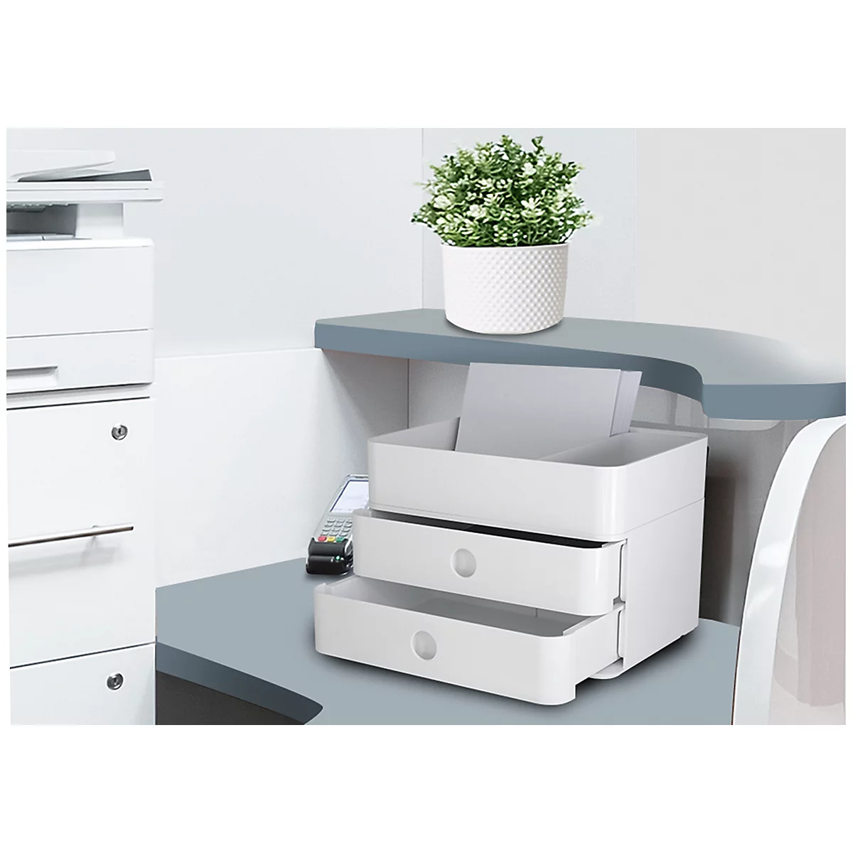 White filing system with two drawers on desk. Plant on top. Printer in the background.
