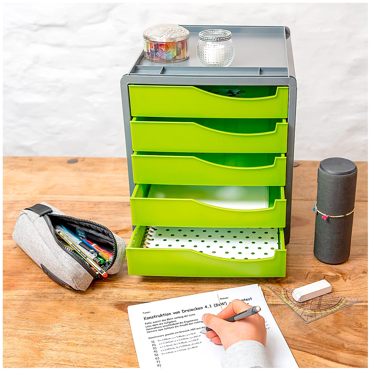 Green drawer cabinet with pens, accessories and a person filling out a form at a desk.