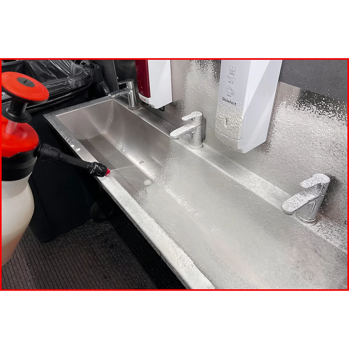Eine Person sprüht Desinfektionsmittel auf ein Waschbecken mit zwei Wasserhähnen.