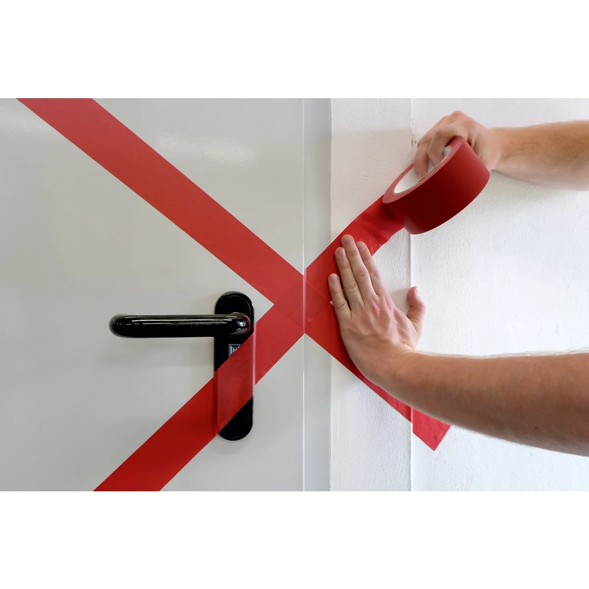 Hands taping a door with red tape. Black door handle.
