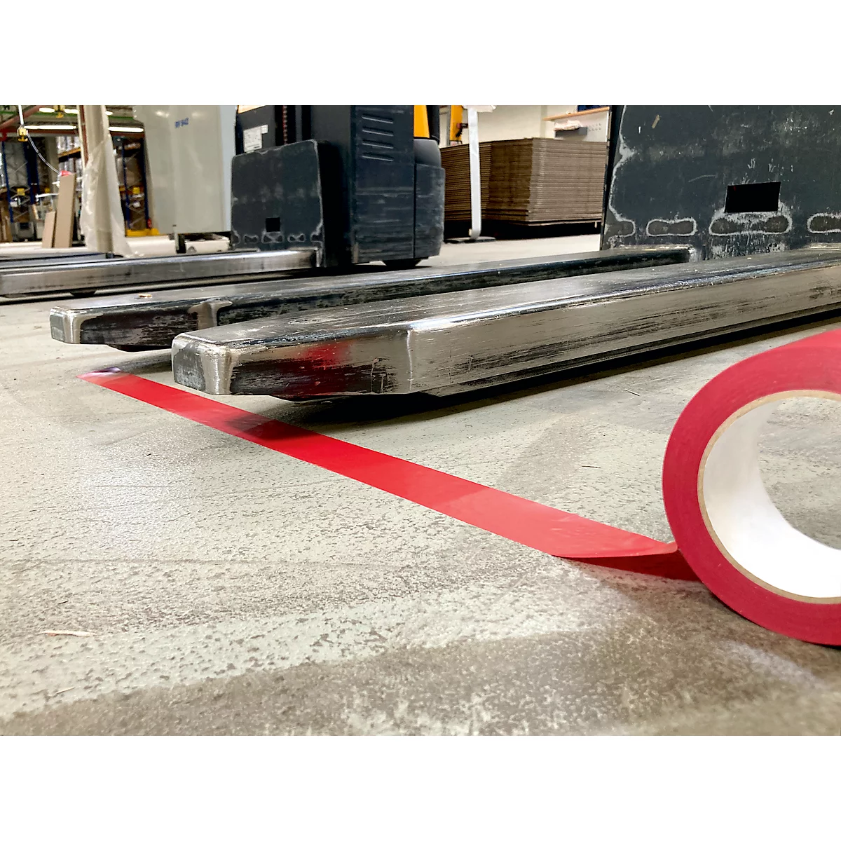 Red tape on concrete floor, forklift in the background.