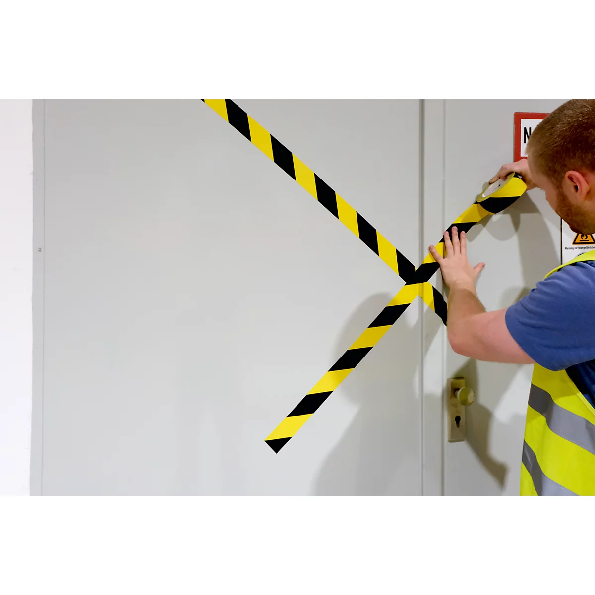 A man applies black and yellow warning tape to a door. The door is closed, and the tape crosses.