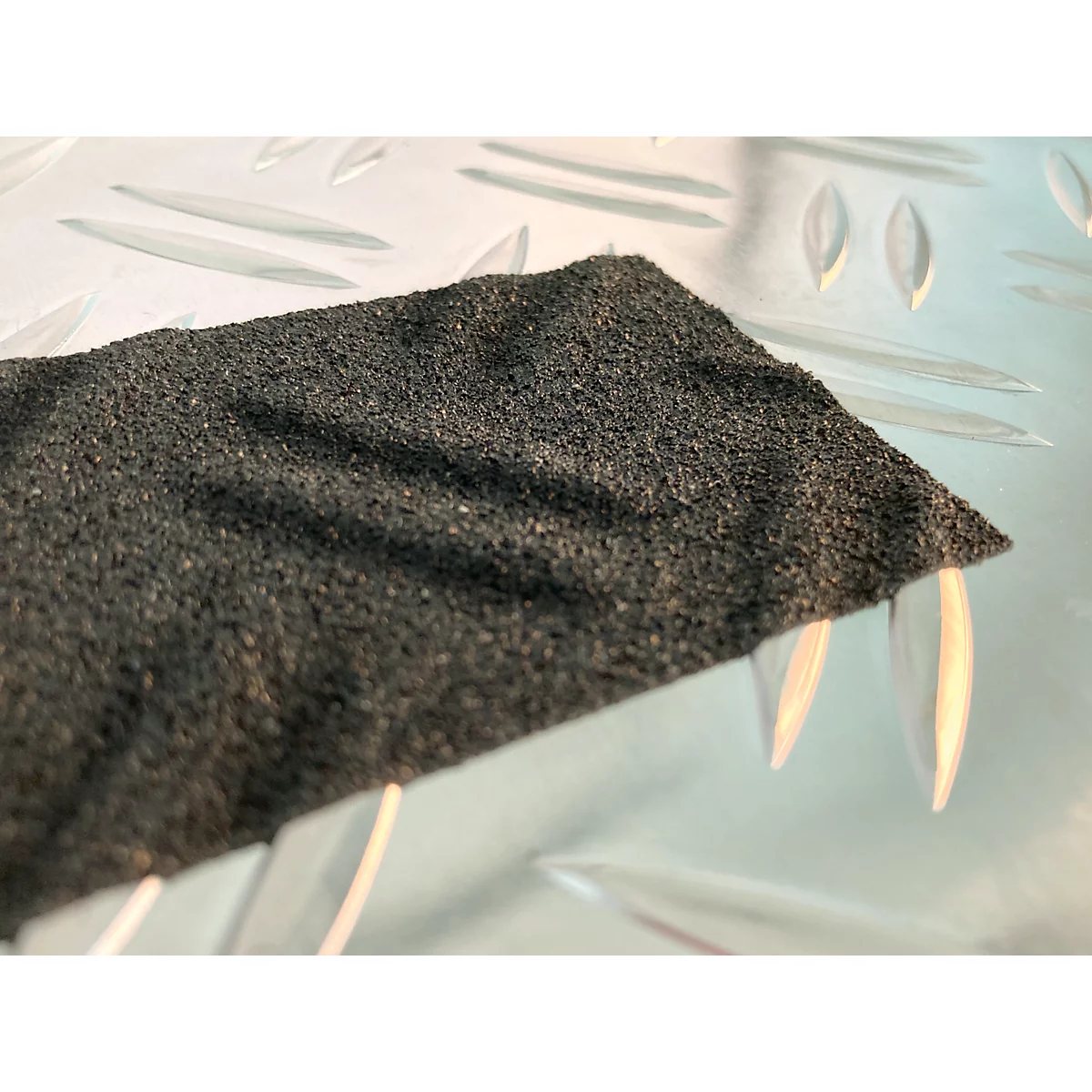 Dark grey, rough material against a smooth, light background. The material has a crumpled surface.