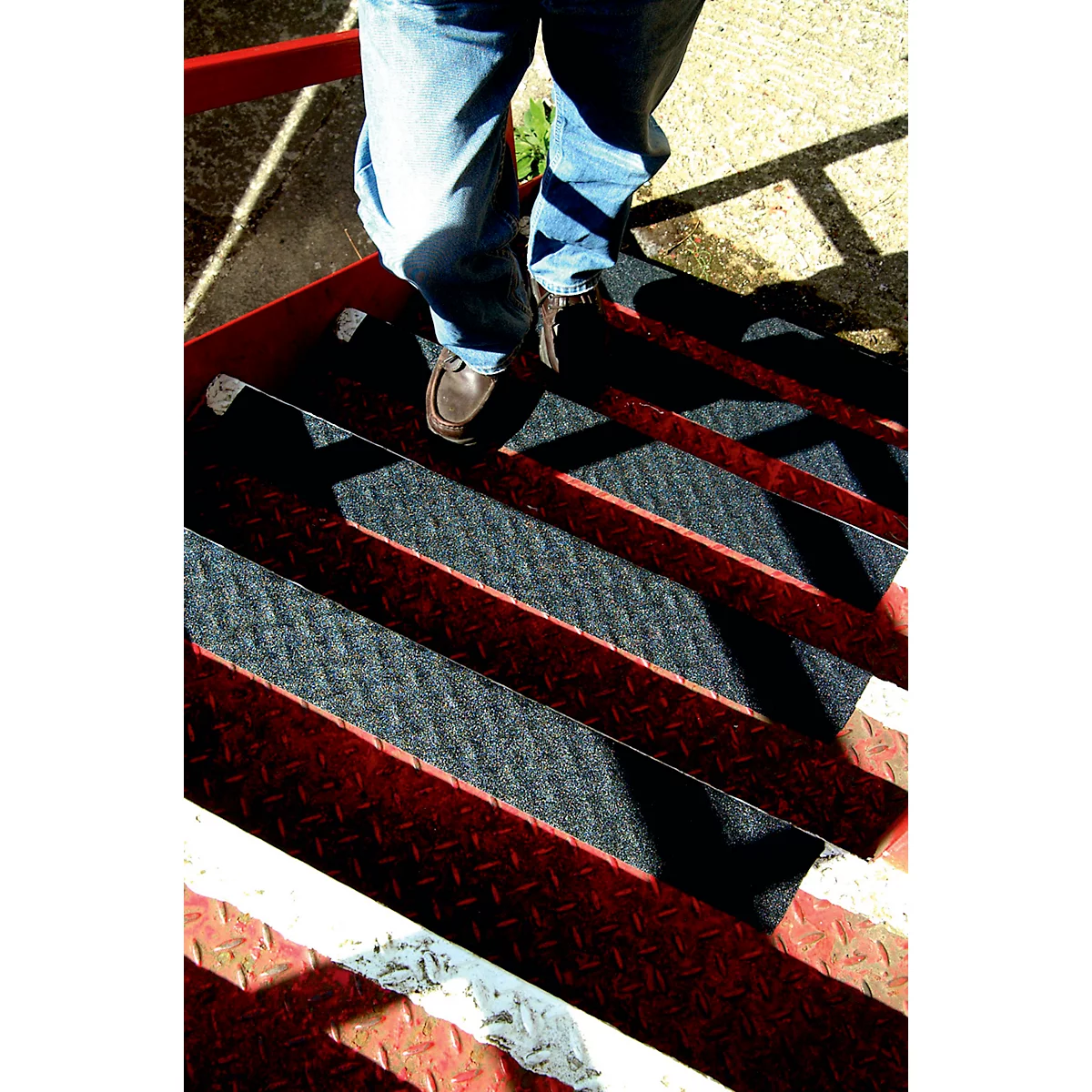 Person standing on metal stairs. The steps are red and black. The person is wearing jeans and brown shoes.