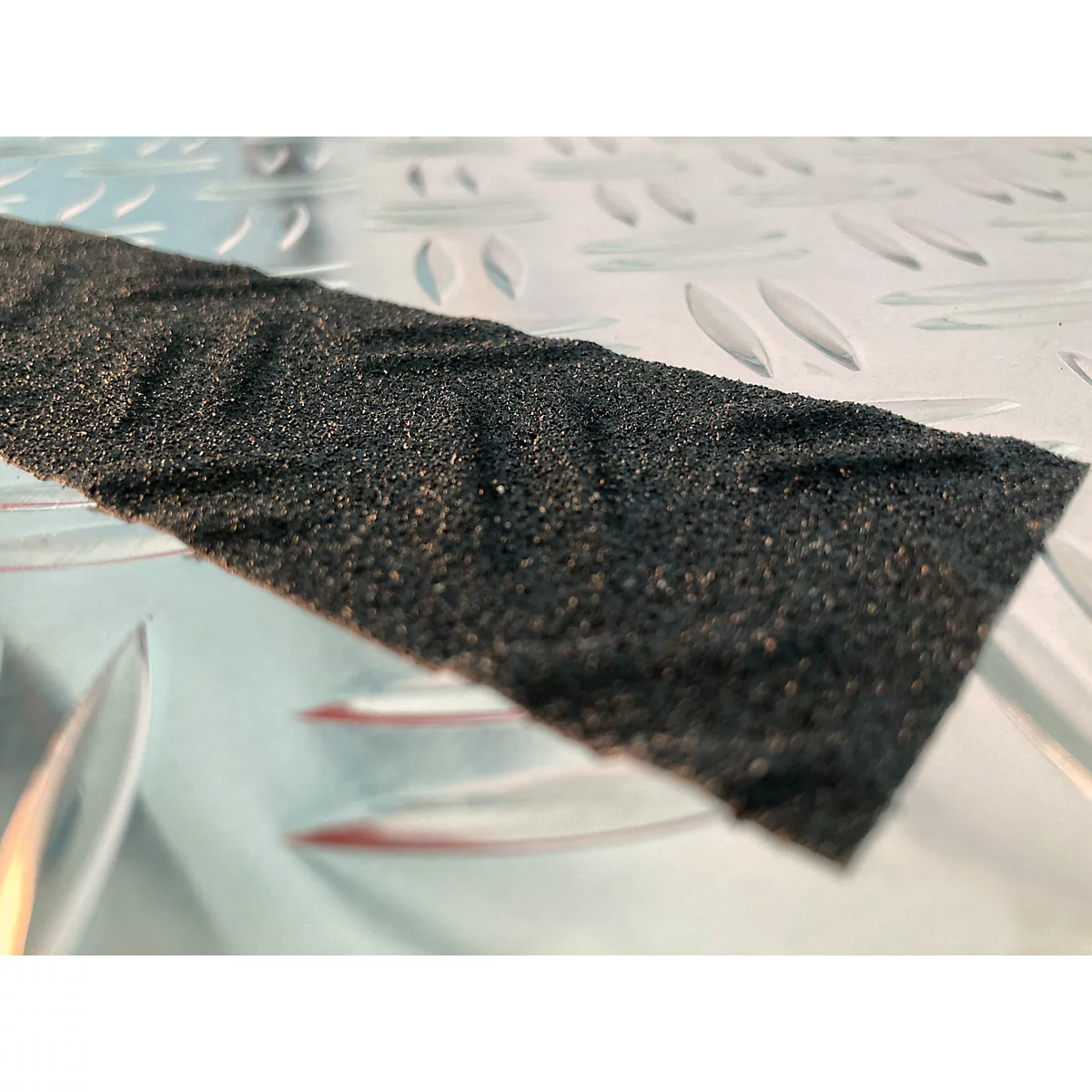 Detail shot of a rough, black tape on a smooth, metallic surface.