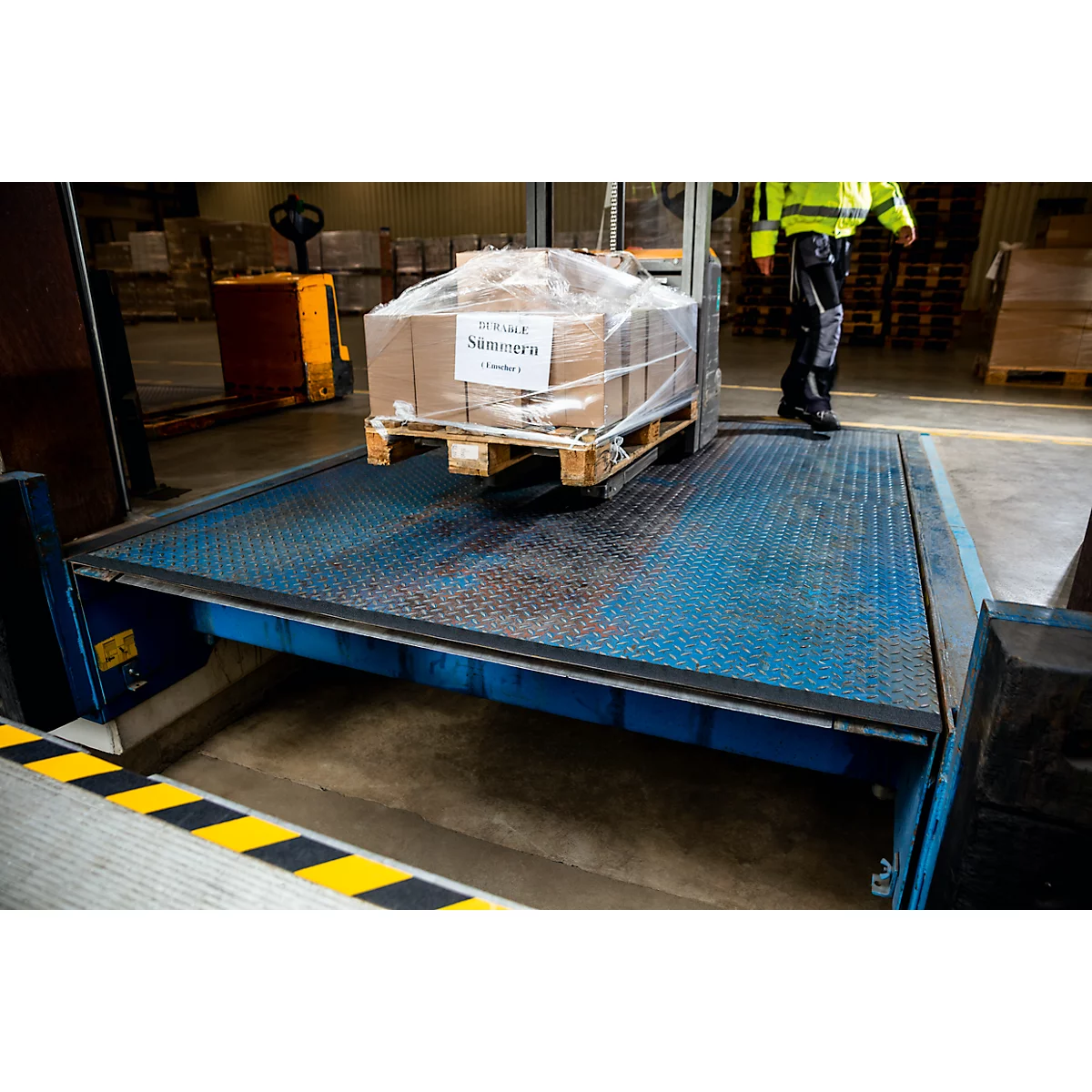 A worker in a yellow jacket loading or unloading boxes on a loading dock.