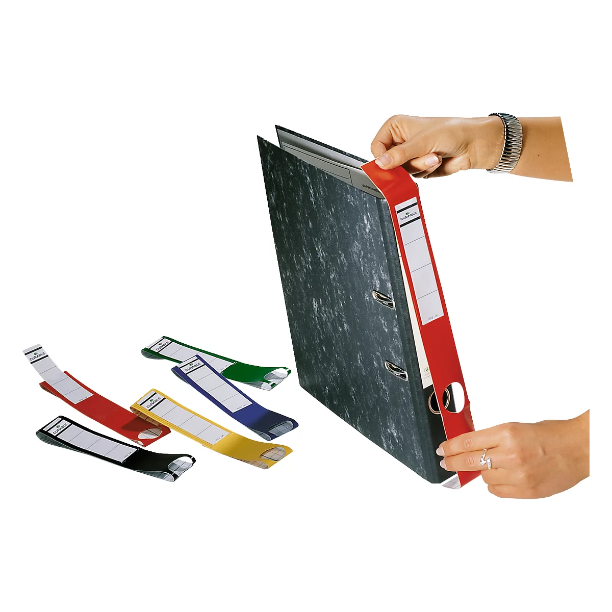 A person holding a red binder with paper labels. Colored labels in red, yellow, green, blue and black are on the table.