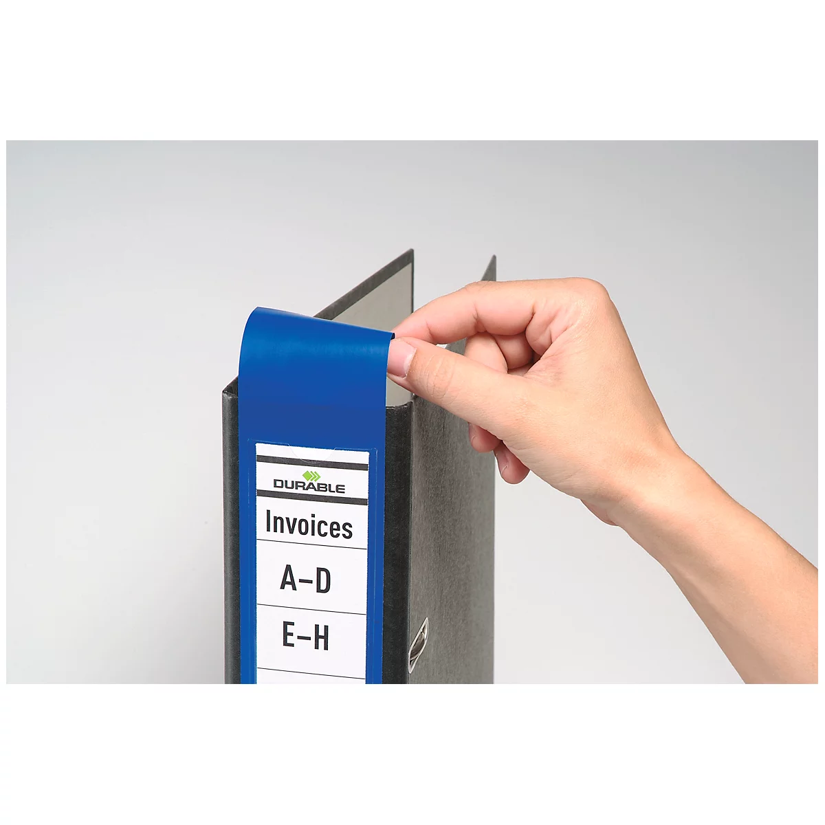 Hand reaching for a blue file folder label with 'Invoices'.